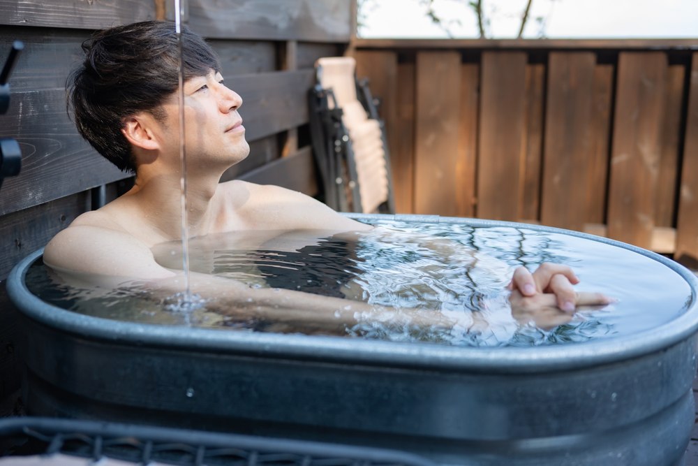 屋外の壺型の浴槽に浸かる男性